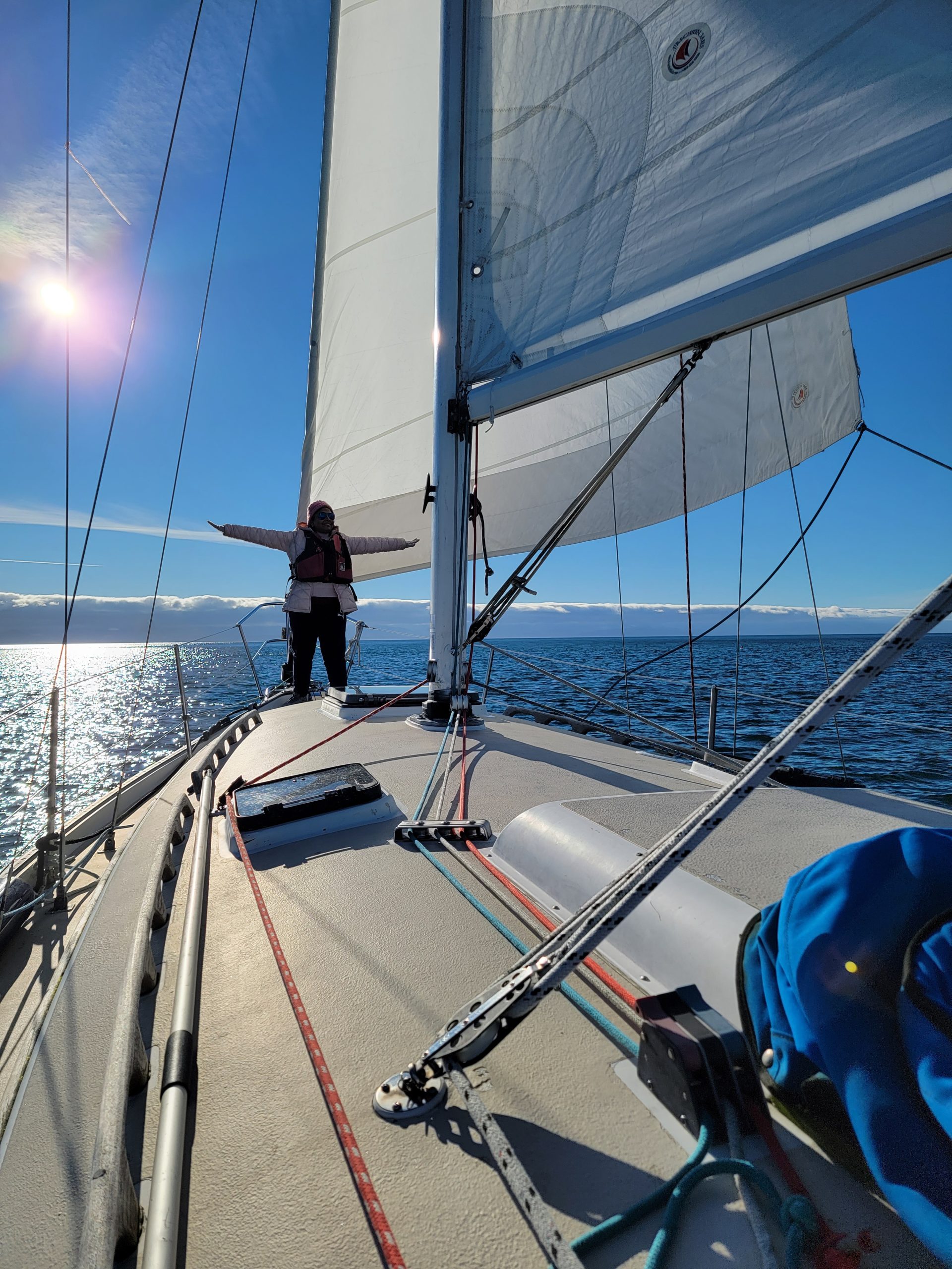 image of the sailboat Starlight with a person standing at the bow with arms out and the sun shining behind